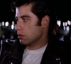 a man in a black leather jacket looking off into the distance with lights behind him