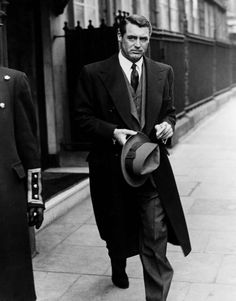 a man in a suit and tie walking down the street with a hat on his shoulder