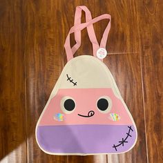 a pink and purple bag with a face on it sitting on a wooden floor next to a brown door