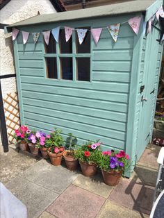 several potted flowers in front of a blue shed with bunting flags on it