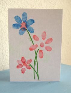 a card with watercolor flowers on it sitting on a blue tablecloth next to a white wall