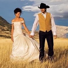 a bride and groom holding hands in the middle of a field with mountains in the background