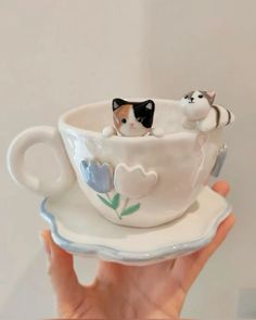 a hand holding a coffee cup with two cats in the top and on the bottom