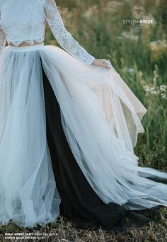 a woman in a white top and black skirt standing in the grass with her hands on her hips