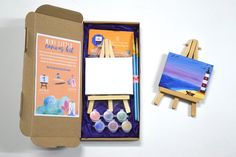 an open box with two easels and some paintbrushes on the table next to it