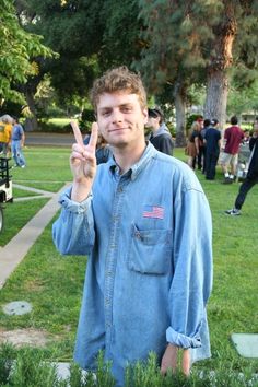 a man standing in the grass holding up his peace sign