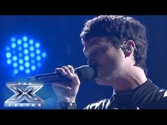 a man singing into a microphone in front of a blue background with the x factor logo