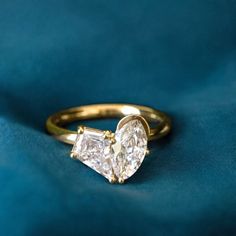 an engagement ring with two pear shaped diamonds on it, sitting on a blue cloth