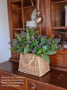 a wicker basket filled with purple flowers on top of a wooden dresser next to a book shelf