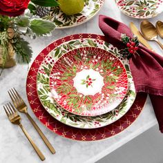 the table is set for christmas dinner with red and green plates, silverware, napkins, and gold flatware