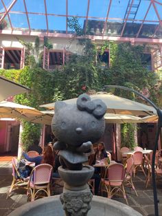 a fountain in the middle of a courtyard with tables and chairs around it, surrounded by greenery