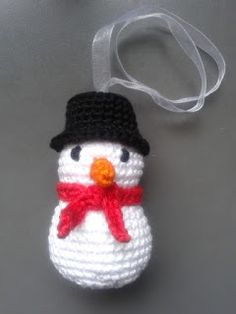 a crocheted snowman ornament hanging from a white ribbon on a gray surface