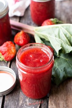 a jar of strawberry jam next to some strawberries and spinach on a wooden table