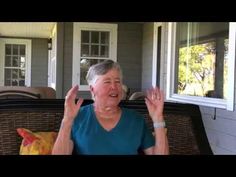 an older woman sitting on a couch in front of a house with her hands up