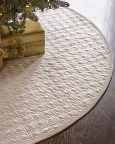 a christmas tree with presents under it on a round table mat in front of a small fir tree