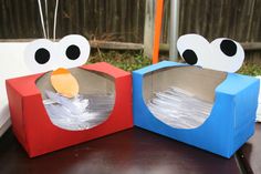 two cardboard boxes with faces on them sitting on a table next to each other, one is empty and the other has paper in it's mouth