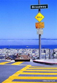 a street sign on top of a pole with other signs below it and the city in the background