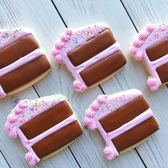 six decorated cookies sitting on top of a white wooden table with pink frosting and sprinkles