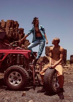 a man sitting on top of a red four wheeler next to another man in the desert