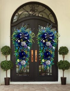 two blue wreaths on the front door of a house with potted plants and trees