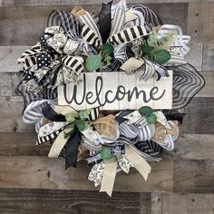 a welcome wreath with black and white ribbons on a wooden background that says, welcome