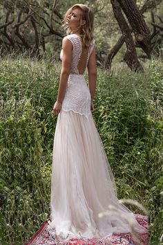 a woman standing on top of a rug in the woods wearing a dress with an open back