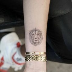 a small lion tattoo on the wrist is shown in black and grey ink with gold chains