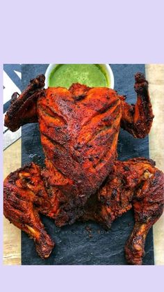 a cooked chicken sitting on top of a cutting board next to a bowl of green sauce