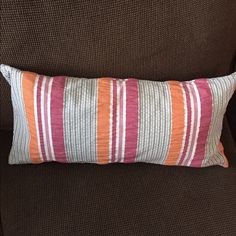 an orange and pink striped pillow sitting on top of a brown couch