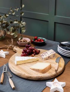 cheese, grapes and crackers sit on a wooden board with star shaped utensils