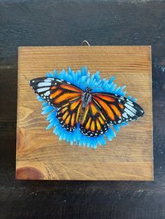 an orange and black butterfly sitting on top of a blue flower in a wooden box