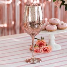 a table topped with pink roses next to donuts and a glass filled with champagne