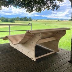 a wooden bench sitting on top of a wooden deck next to a tree and green field