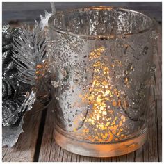 a glass candle holder sitting on top of a wooden table next to a pine cone