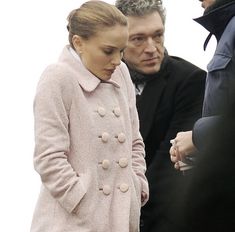 a man and woman standing next to each other in front of some people wearing coats