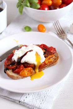 a white plate topped with an open face sandwich next to a bowl of cherry tomatoes