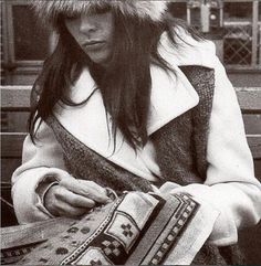 a woman sitting on a bench wearing a fur hat and looking at her cell phone