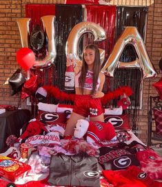 a young woman sitting on top of a bed surrounded by red and black decorations, balloons and letters