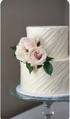 a wedding cake with white frosting and pink roses on top is sitting on a glass plate