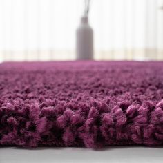 a purple rug is on the floor in front of a white vase and window with curtains