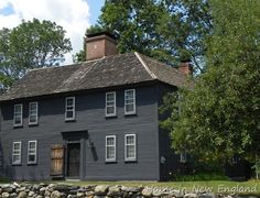 an old black house with stone walls and trees in the foreground, on a sunny day