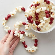 a bowl of popcorn with cranberries and nuts on the table next to it