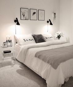 a bedroom with white walls and grey carpeted flooring, two framed pictures on the wall above the bed