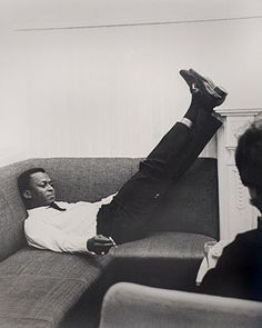 a black and white photo of a man laying on a couch with his feet up