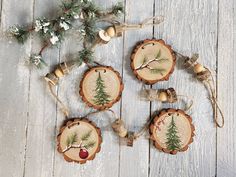 three wooden ornaments with pine trees and bells hanging from them on a white wood background