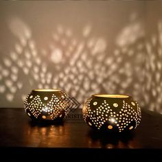 two lit candles are sitting on a table in front of a wall with shadows cast onto it