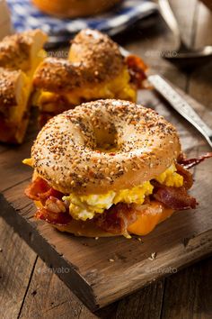 a bagel sandwich with bacon, cheese and eggs on a cutting board next to a knife