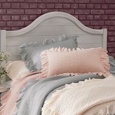 a white bed with pink and grey pillows on top of it next to a brick wall