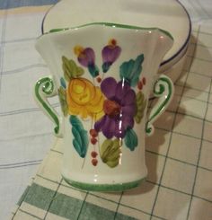 a white pitcher with flowers painted on it sitting on a checkered tablecloth covered table