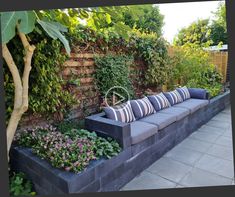 a couch sitting in the middle of a garden next to a wall with plants on it